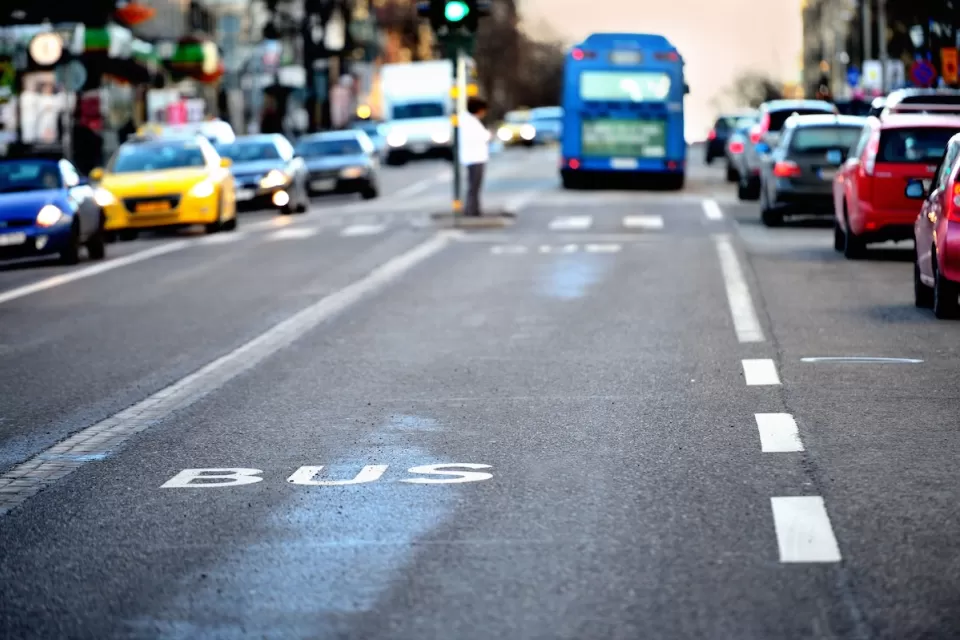 Close-up of white BUS letters on asphalt bus lane with blurred bus and traffic in background.